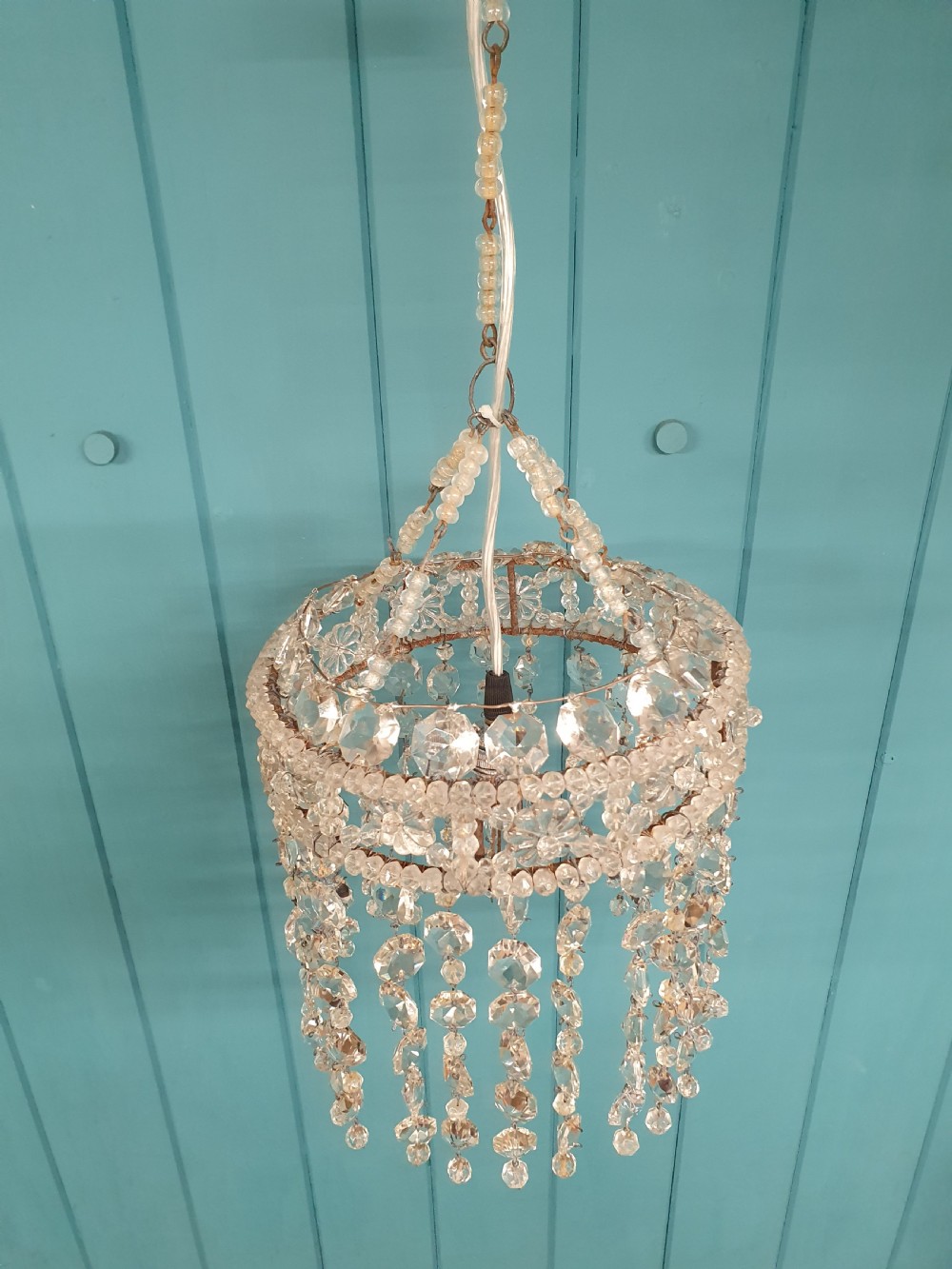 A small cylindrical ceiling light shade constructed from clear glass beads on a wire frame, featuring floral pattern bands and cascading faceted bead strands. View V