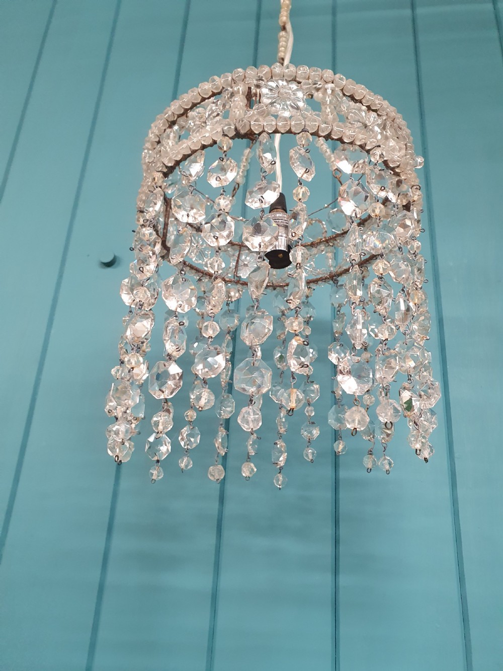 A small cylindrical ceiling light shade constructed from clear glass beads on a wire frame, featuring floral pattern bands and cascading faceted bead strands. View VI