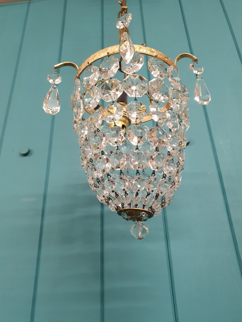 An early 20th-century small crystal bag chandelier featuring a brass filigree upper rim and faceted glass drops suspended from a brass chain. View IV