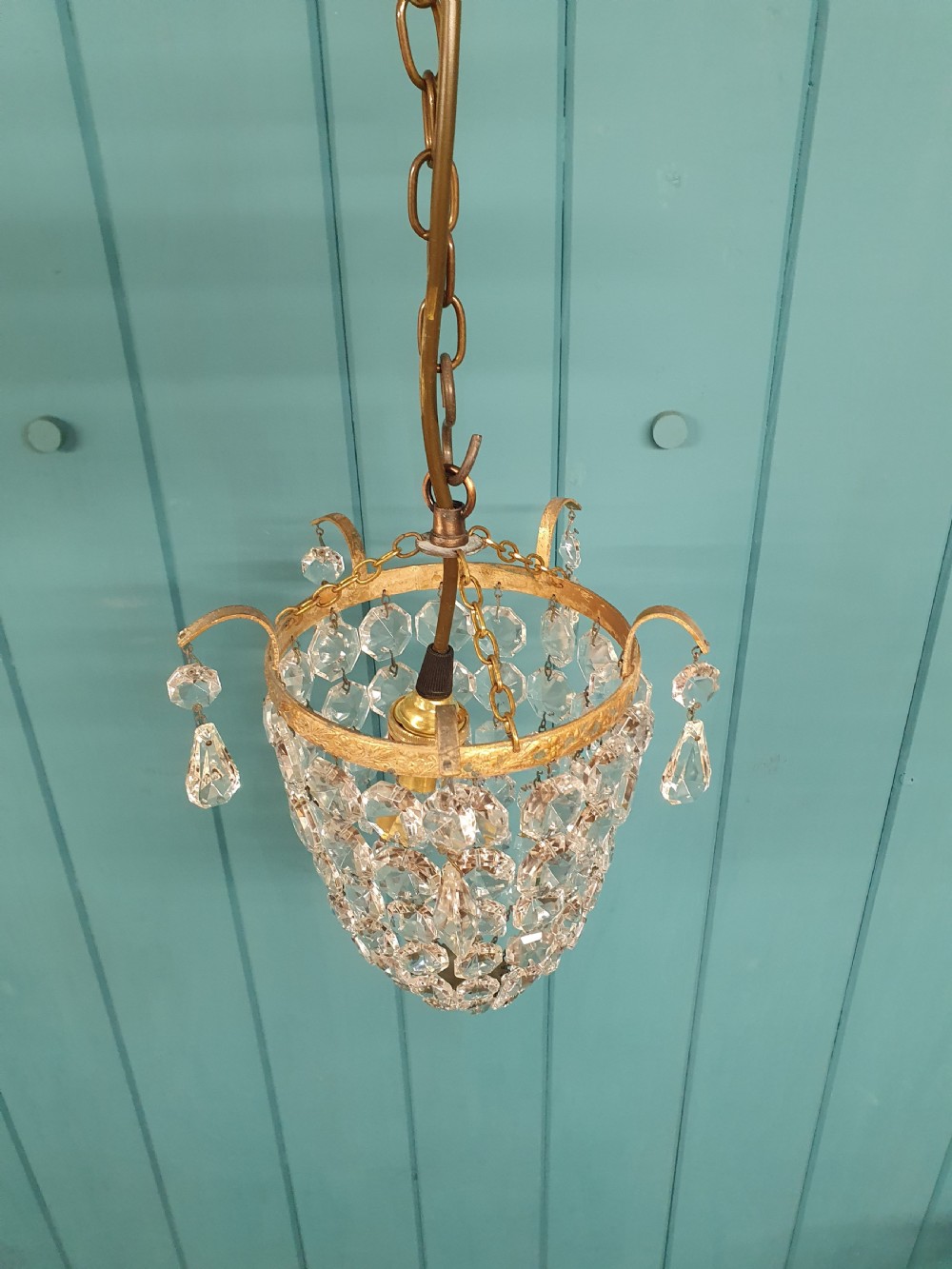An early 20th-century small crystal bag chandelier featuring a brass filigree upper rim and faceted glass drops suspended from a brass chain. View VI