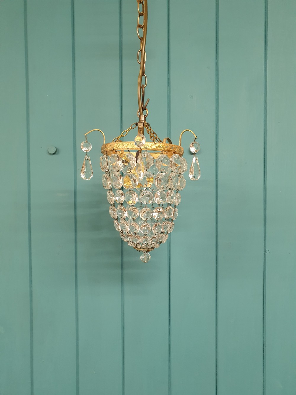 An early 20th-century small crystal bag chandelier featuring a brass filigree upper rim and faceted glass drops suspended from a brass chain. View VIII