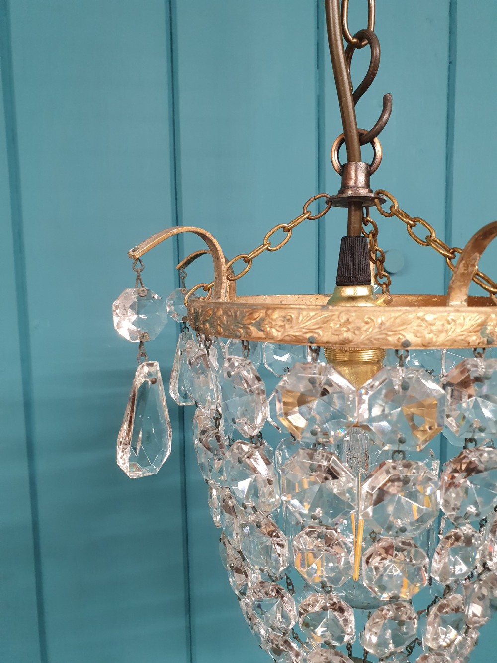 An early 20th-century small crystal bag chandelier featuring a brass filigree upper rim and faceted glass drops suspended from a brass chain. View X