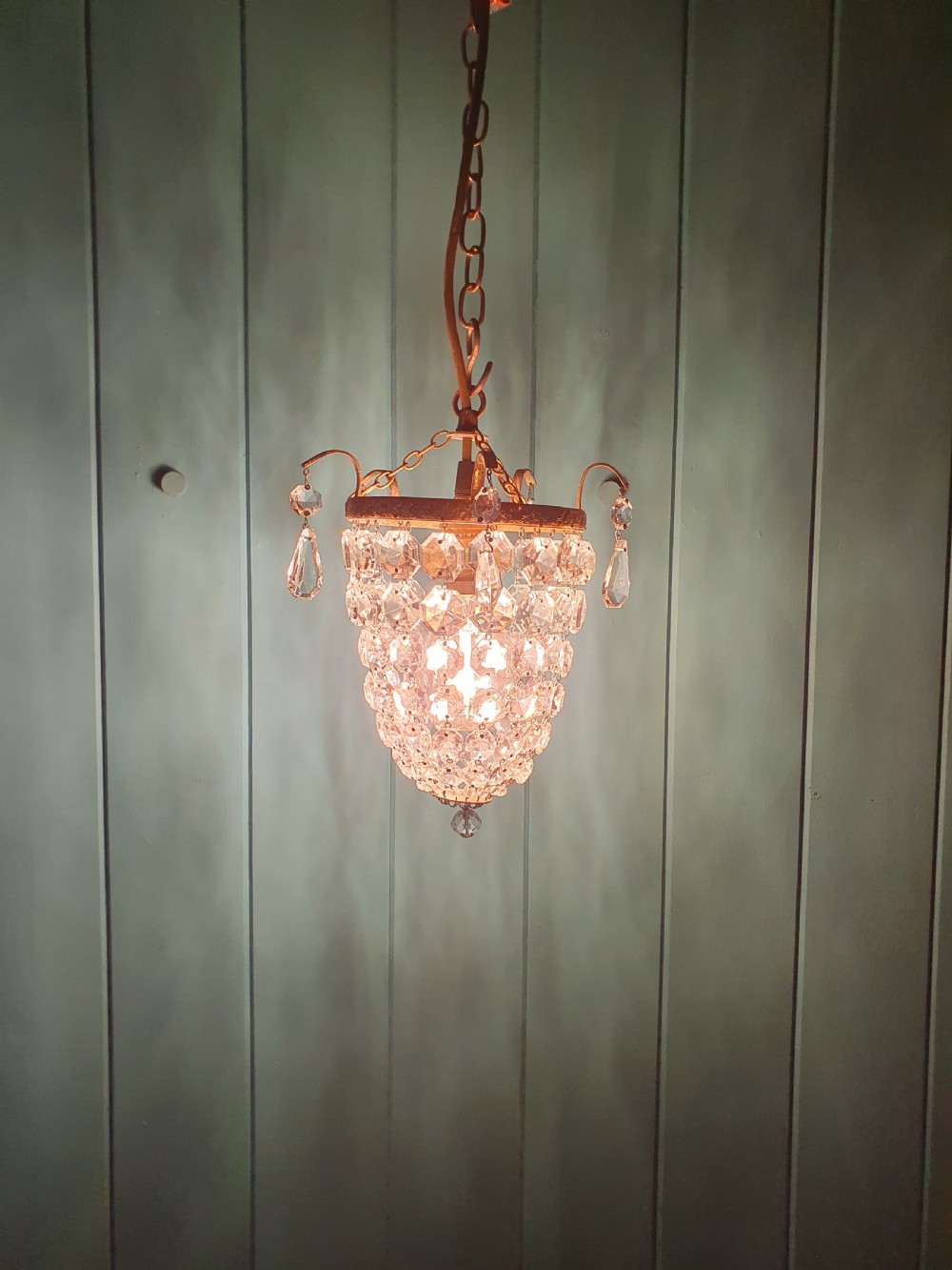 An early 20th-century small crystal bag chandelier featuring a brass filigree upper rim and faceted glass drops suspended from a brass chain. View XII