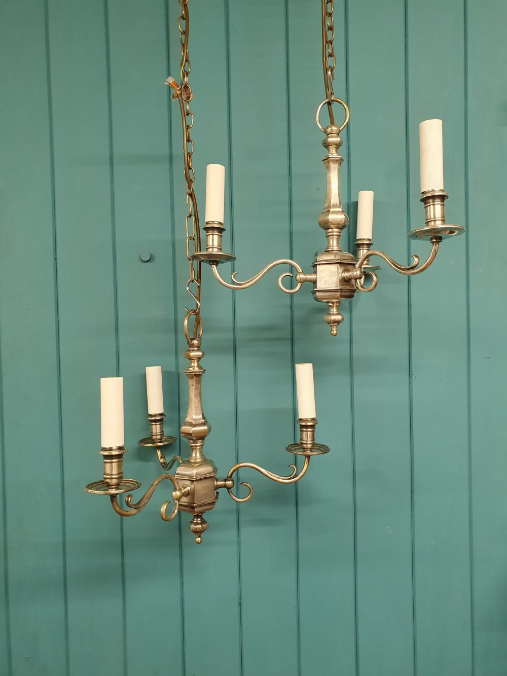 A pair of early twentieth-century nickel silver chandeliers, each featuring a central baluster stem, three scrolling arms, and candle-style lamp holders.