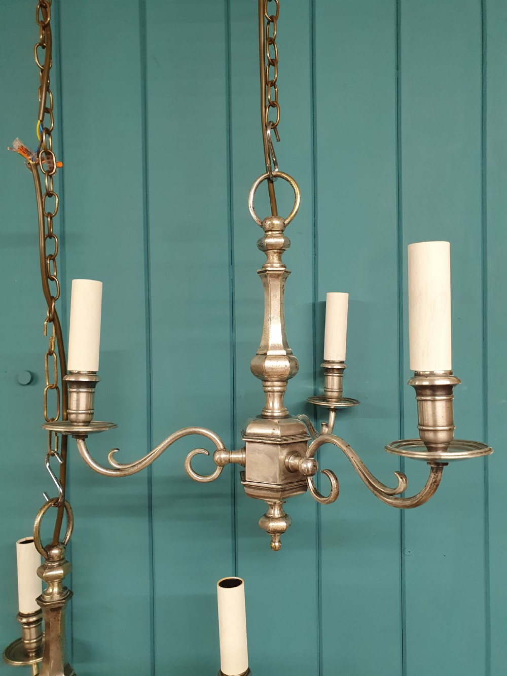 A pair of early twentieth-century nickel silver chandeliers, each featuring a central baluster stem, three scrolling arms, and candle-style lamp holders. View VI