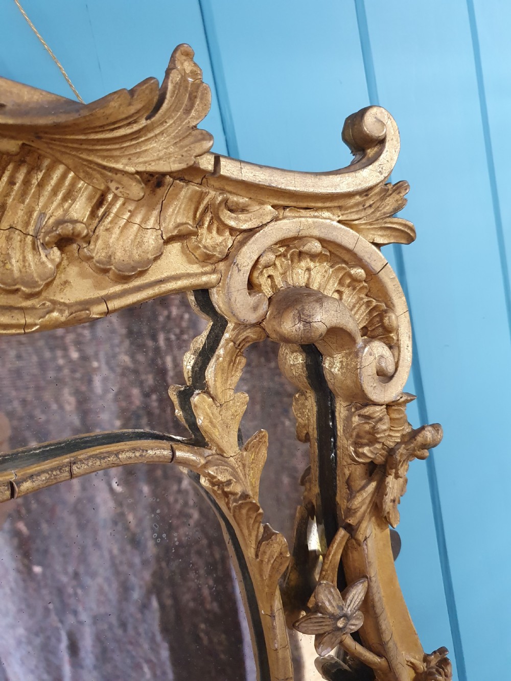 An ornate 19th-century Rococo style giltwood wall mirror featuring carved floral accents, scrollwork, and a decorative inner frame boundary. View V