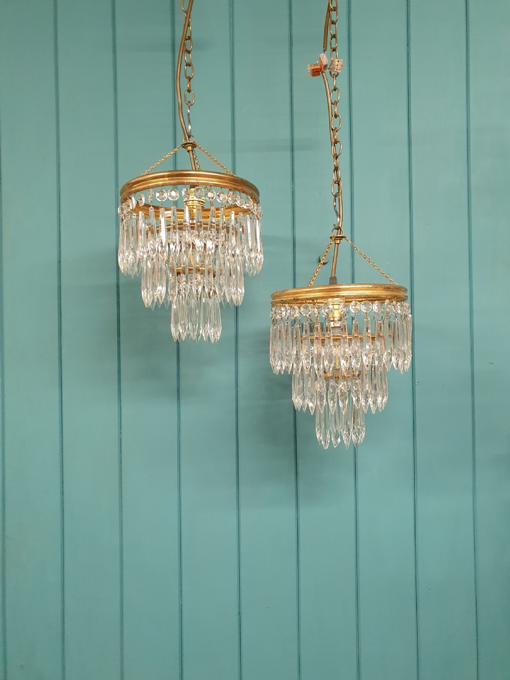 A pair of early 20th-century brass pendant chandeliers featuring tiered hanging crystal spikes suspended by linked chains.