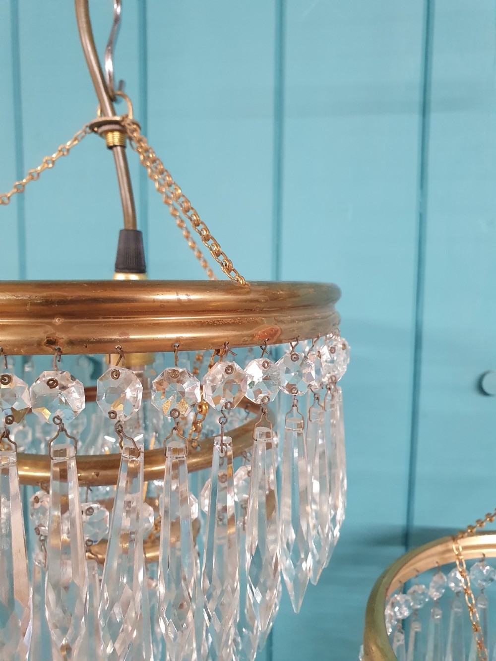 A pair of early 20th-century brass pendant chandeliers featuring tiered hanging crystal spikes suspended by linked chains. View II