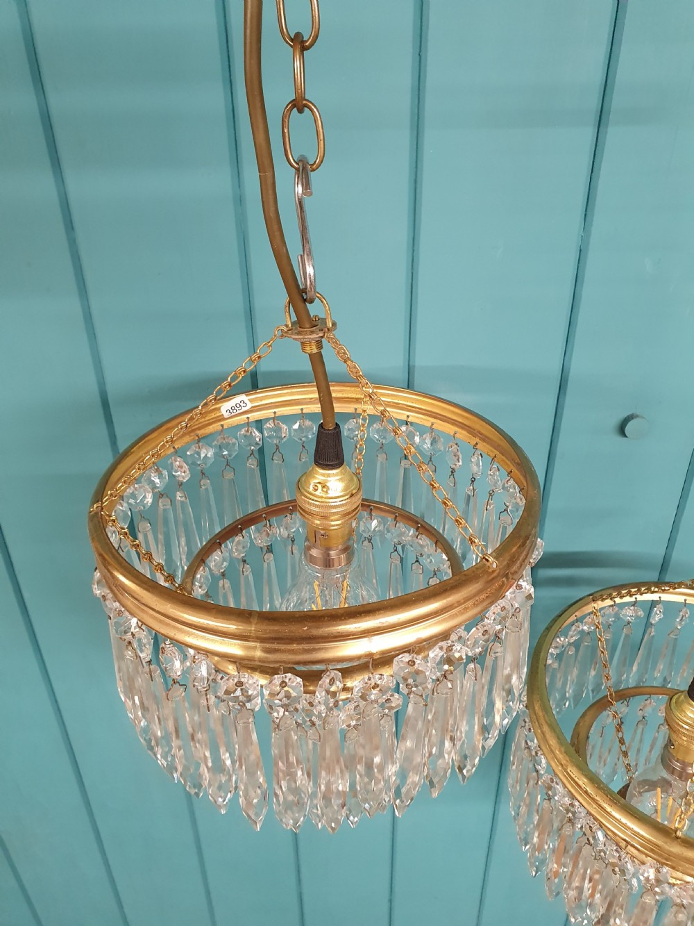 A pair of early 20th-century brass pendant chandeliers featuring tiered hanging crystal spikes suspended by linked chains. View IV