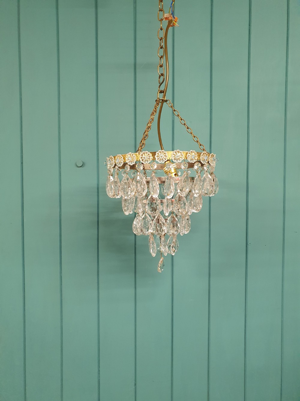 An early 20th-century tiered drip chandelier featuring cascading glass crystal teardrops suspended from a brass floral band and hanging chain.