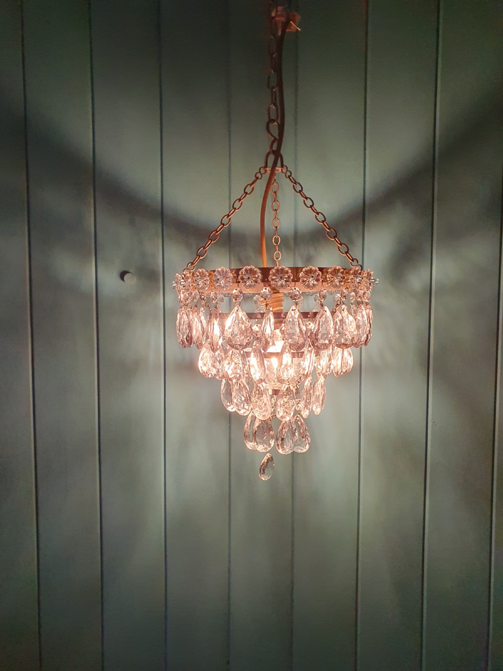 An early 20th-century tiered drip chandelier featuring cascading glass crystal teardrops suspended from a brass floral band and hanging chain. View II
