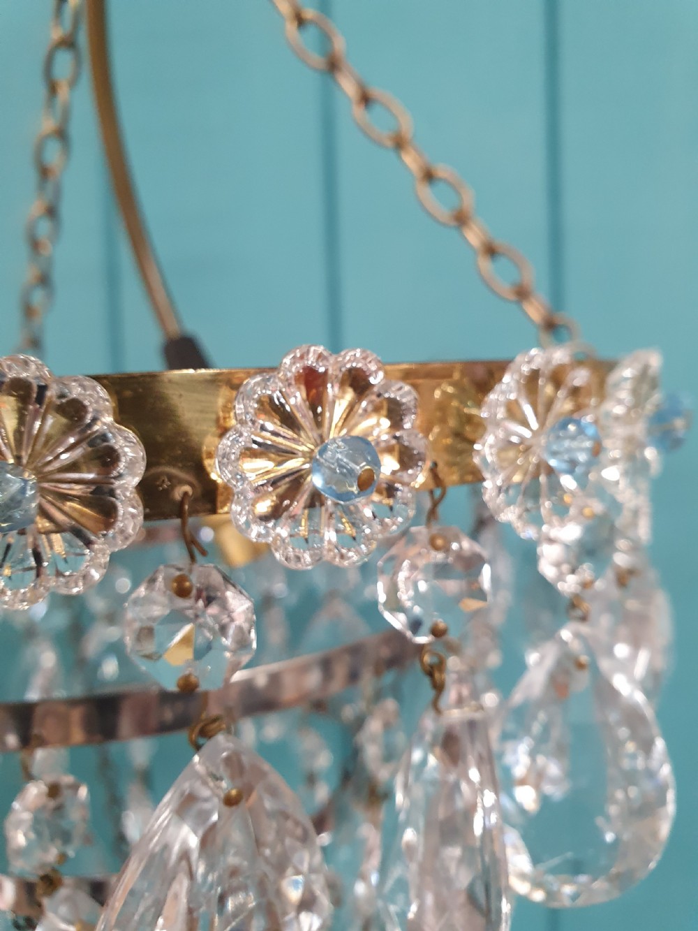An early 20th-century tiered drip chandelier featuring cascading glass crystal teardrops suspended from a brass floral band and hanging chain. View III
