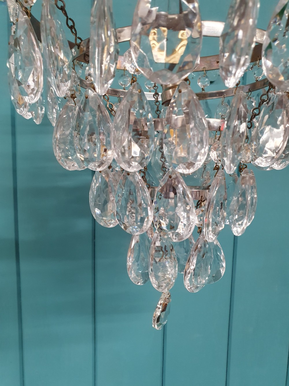 An early 20th-century tiered drip chandelier featuring cascading glass crystal teardrops suspended from a brass floral band and hanging chain. View IV