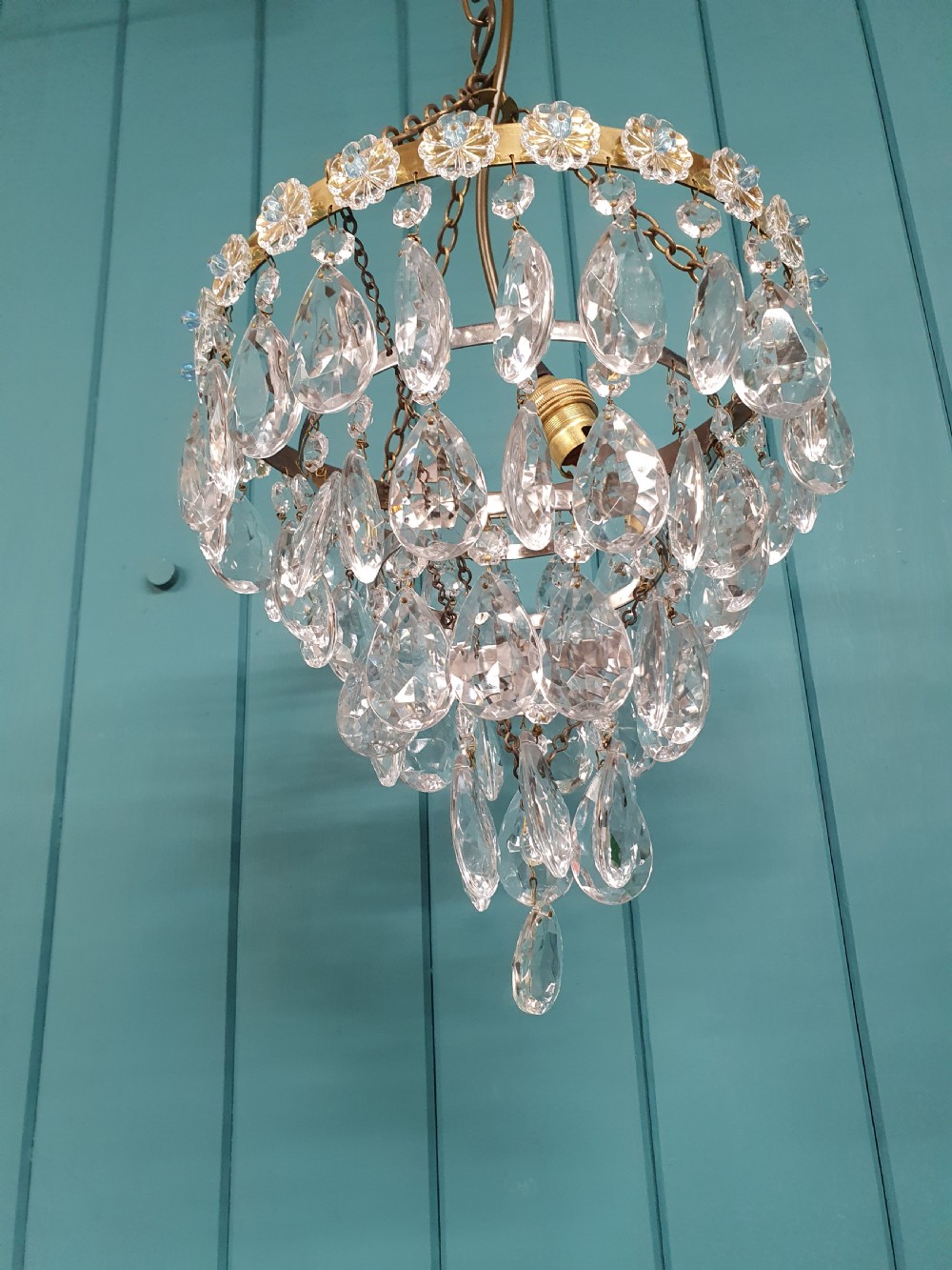 An early 20th-century tiered drip chandelier featuring cascading glass crystal teardrops suspended from a brass floral band and hanging chain. View V
