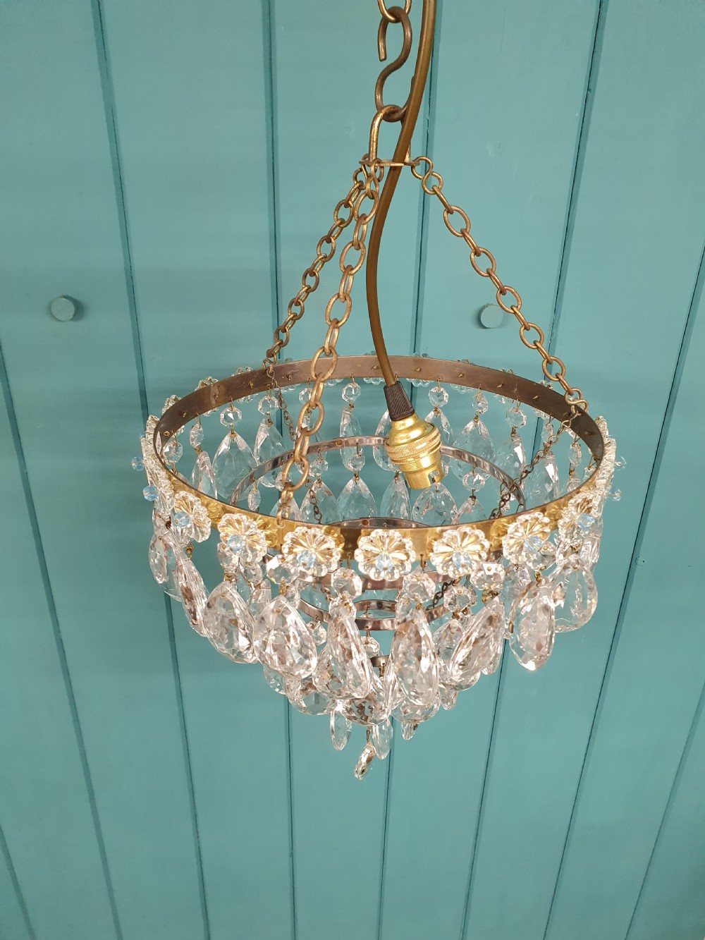 An early 20th-century tiered drip chandelier featuring cascading glass crystal teardrops suspended from a brass floral band and hanging chain. View VI