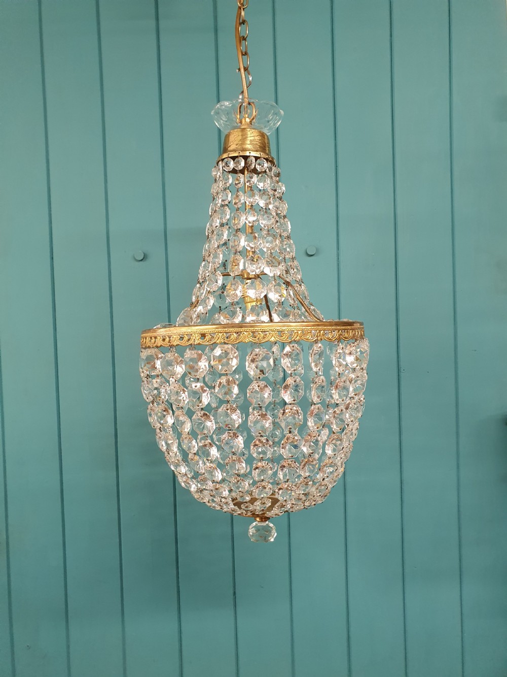 An antique brass tent and bag chandelier featuring rows of faceted glass crystals strung into an upper cone and lower rounded basket hanging from a brass chain.