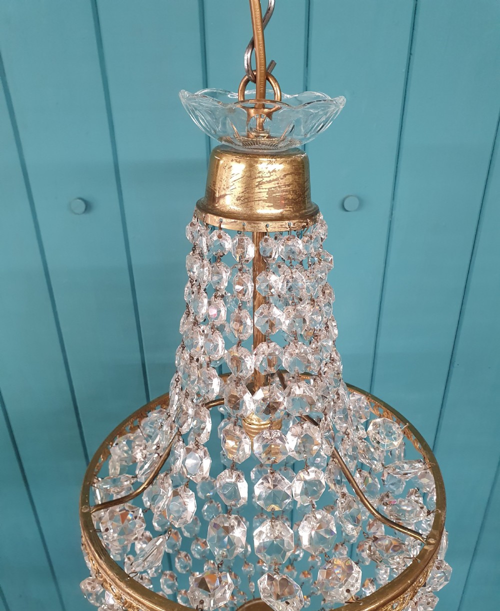 An antique brass tent and bag chandelier featuring rows of faceted glass crystals strung into an upper cone and lower rounded basket hanging from a brass chain. View II