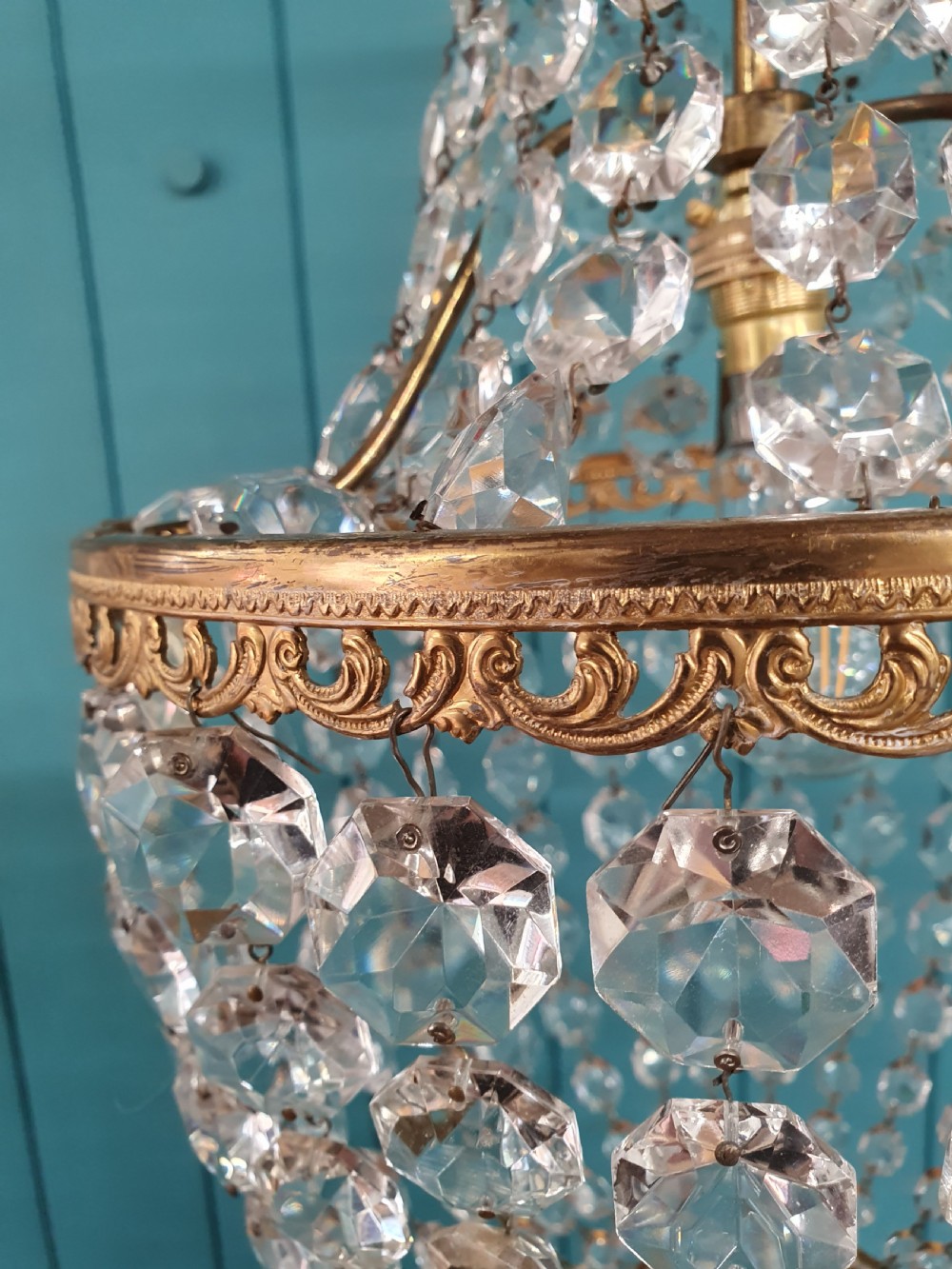 An antique brass tent and bag chandelier featuring rows of faceted glass crystals strung into an upper cone and lower rounded basket hanging from a brass chain. View III