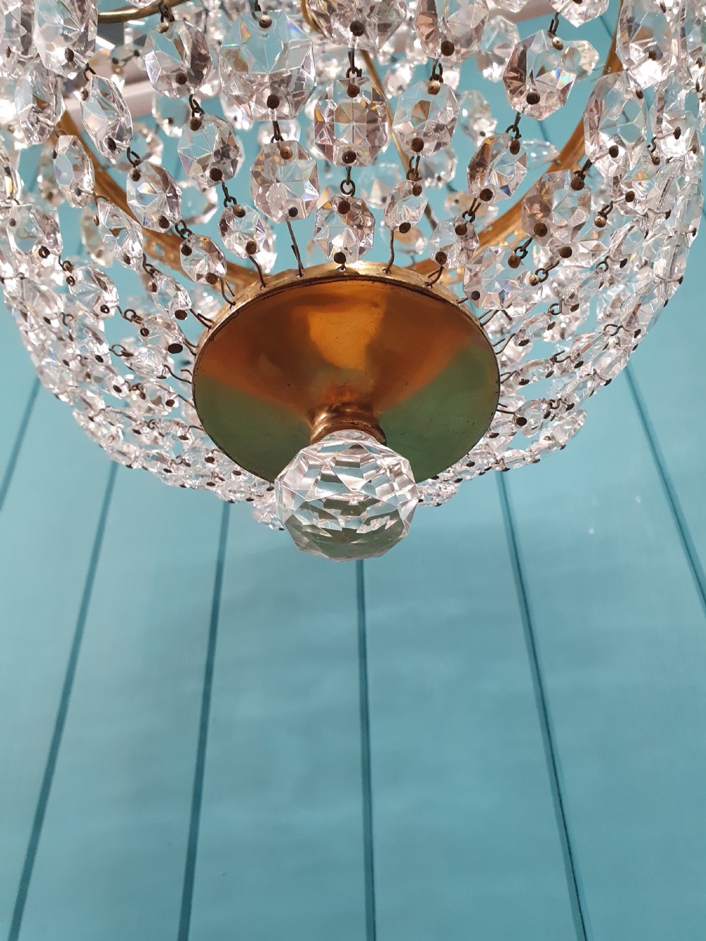 An antique brass tent and bag chandelier featuring rows of faceted glass crystals strung into an upper cone and lower rounded basket hanging from a brass chain. View IV
