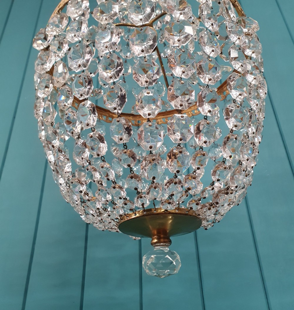 An antique brass tent and bag chandelier featuring rows of faceted glass crystals strung into an upper cone and lower rounded basket hanging from a brass chain. View V