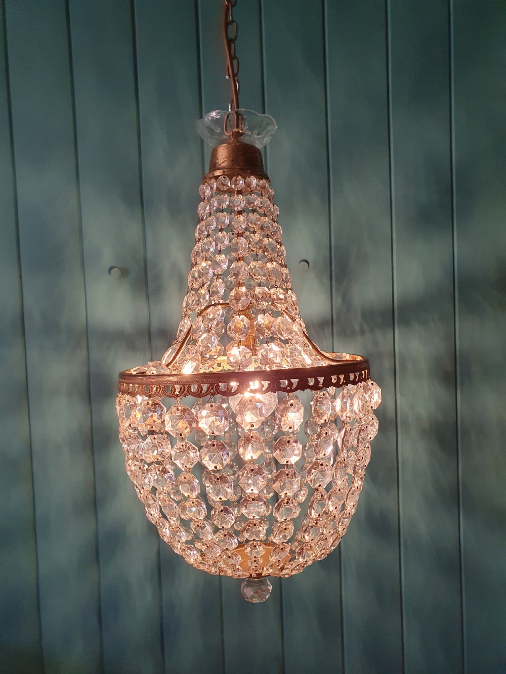 An antique brass tent and bag chandelier featuring rows of faceted glass crystals strung into an upper cone and lower rounded basket hanging from a brass chain. View VI