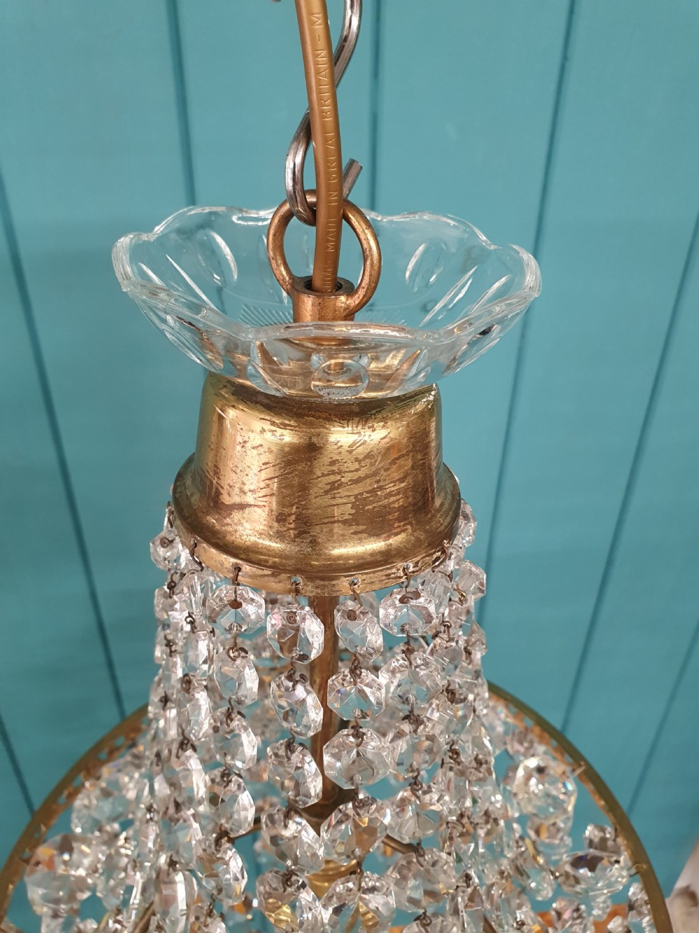 An antique brass tent and bag chandelier featuring rows of faceted glass crystals strung into an upper cone and lower rounded basket hanging from a brass chain. View VII