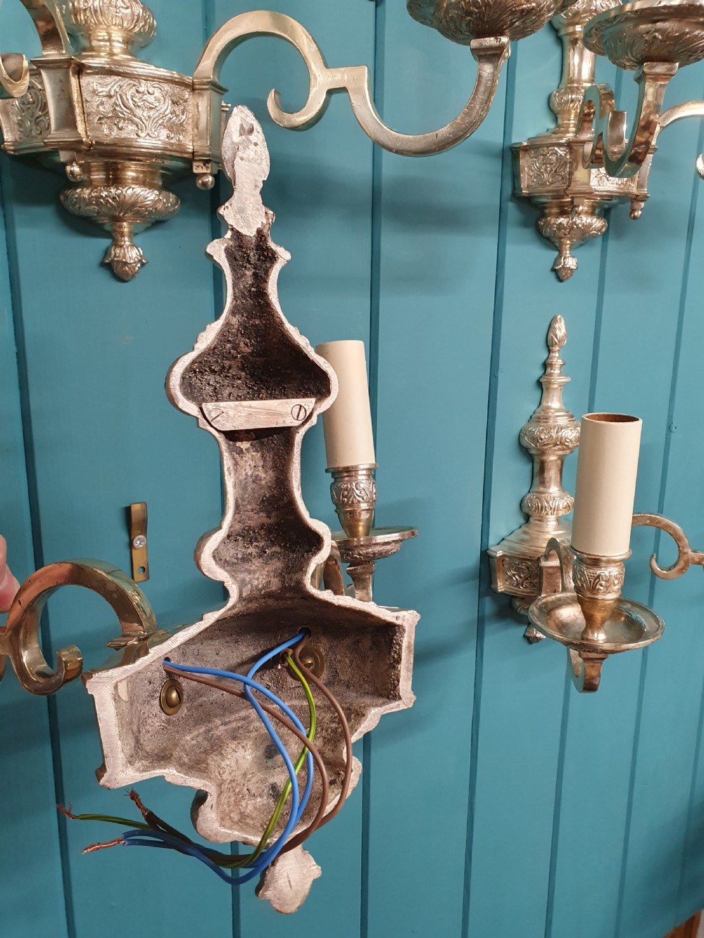 Set of seven silver-plated twin-branch wall lights featuring relief-carved backplates, urn finials, twin scroll arms, and faux candle sleeves. View III