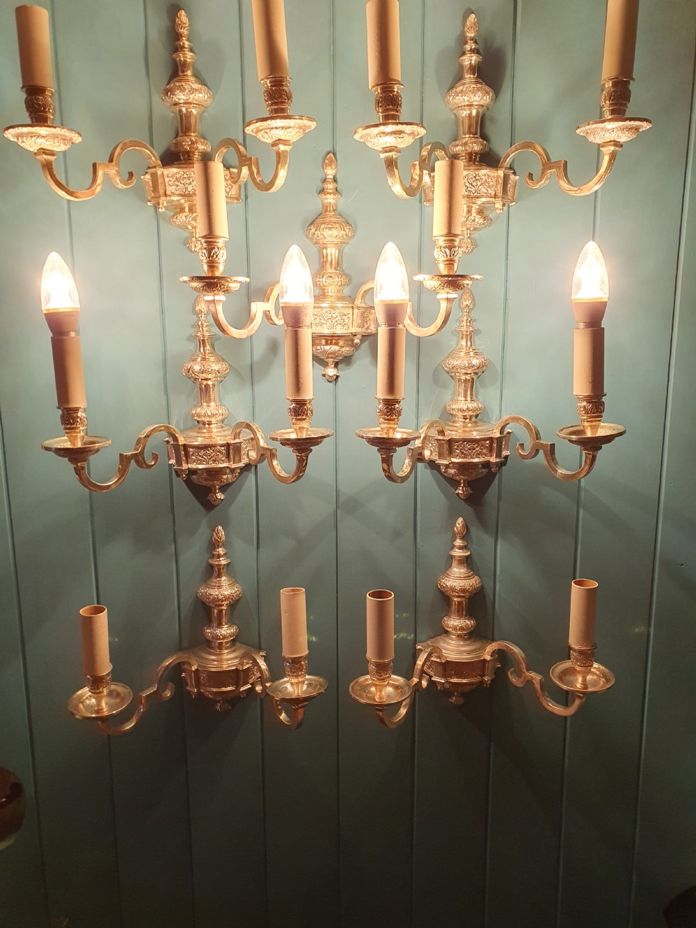 Set of seven silver-plated twin-branch wall lights featuring relief-carved backplates, urn finials, twin scroll arms, and faux candle sleeves. View IV