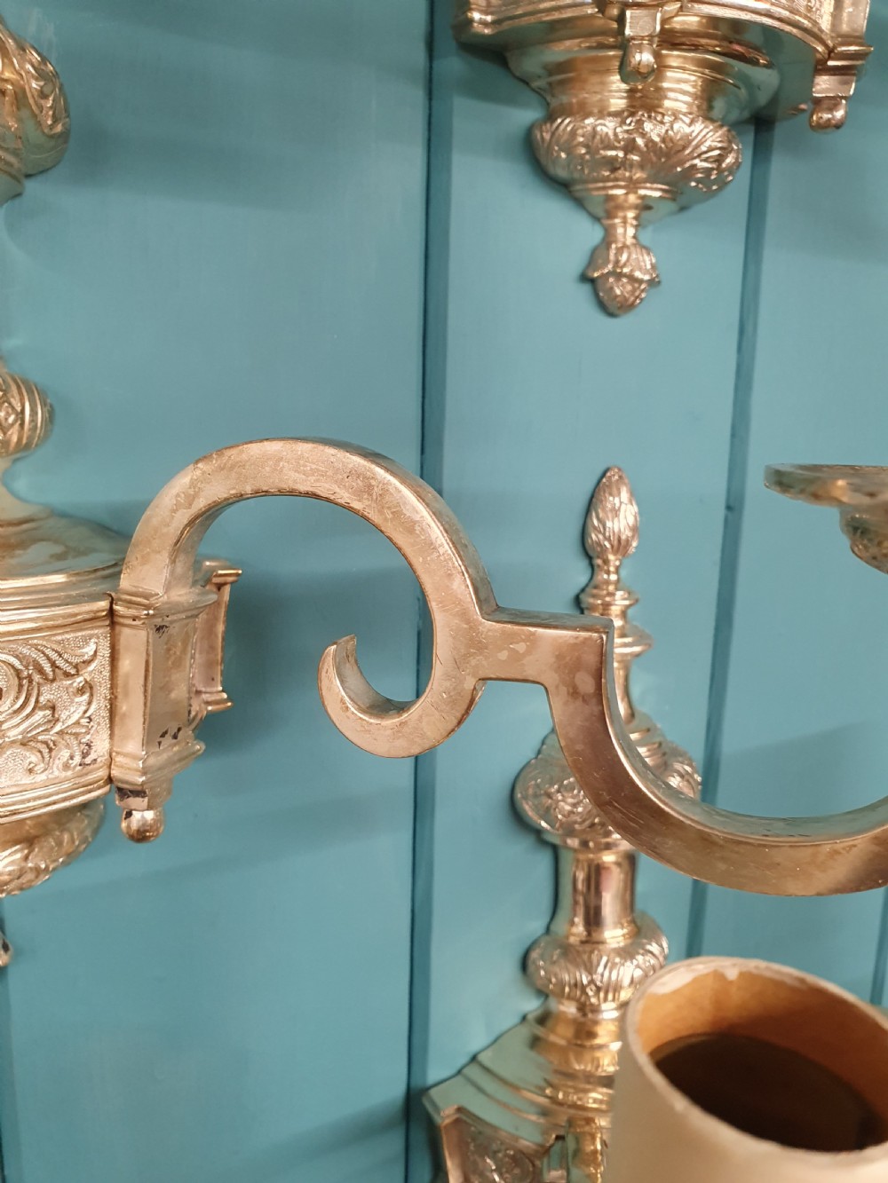 Set of seven silver-plated twin-branch wall lights featuring relief-carved backplates, urn finials, twin scroll arms, and faux candle sleeves. View VII