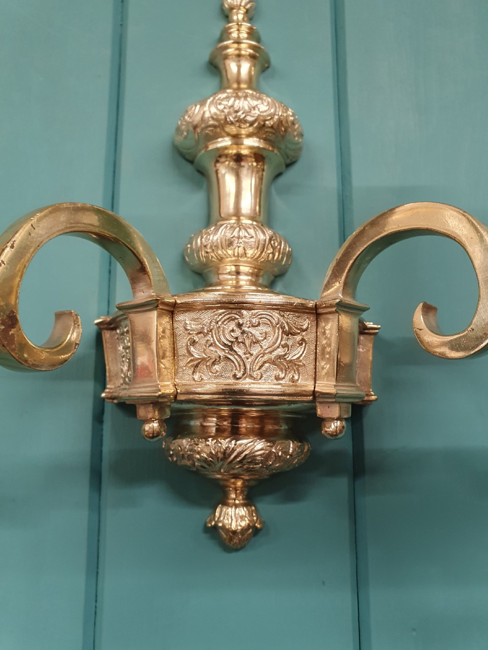 Set of seven silver-plated twin-branch wall lights featuring relief-carved backplates, urn finials, twin scroll arms, and faux candle sleeves. View VIII