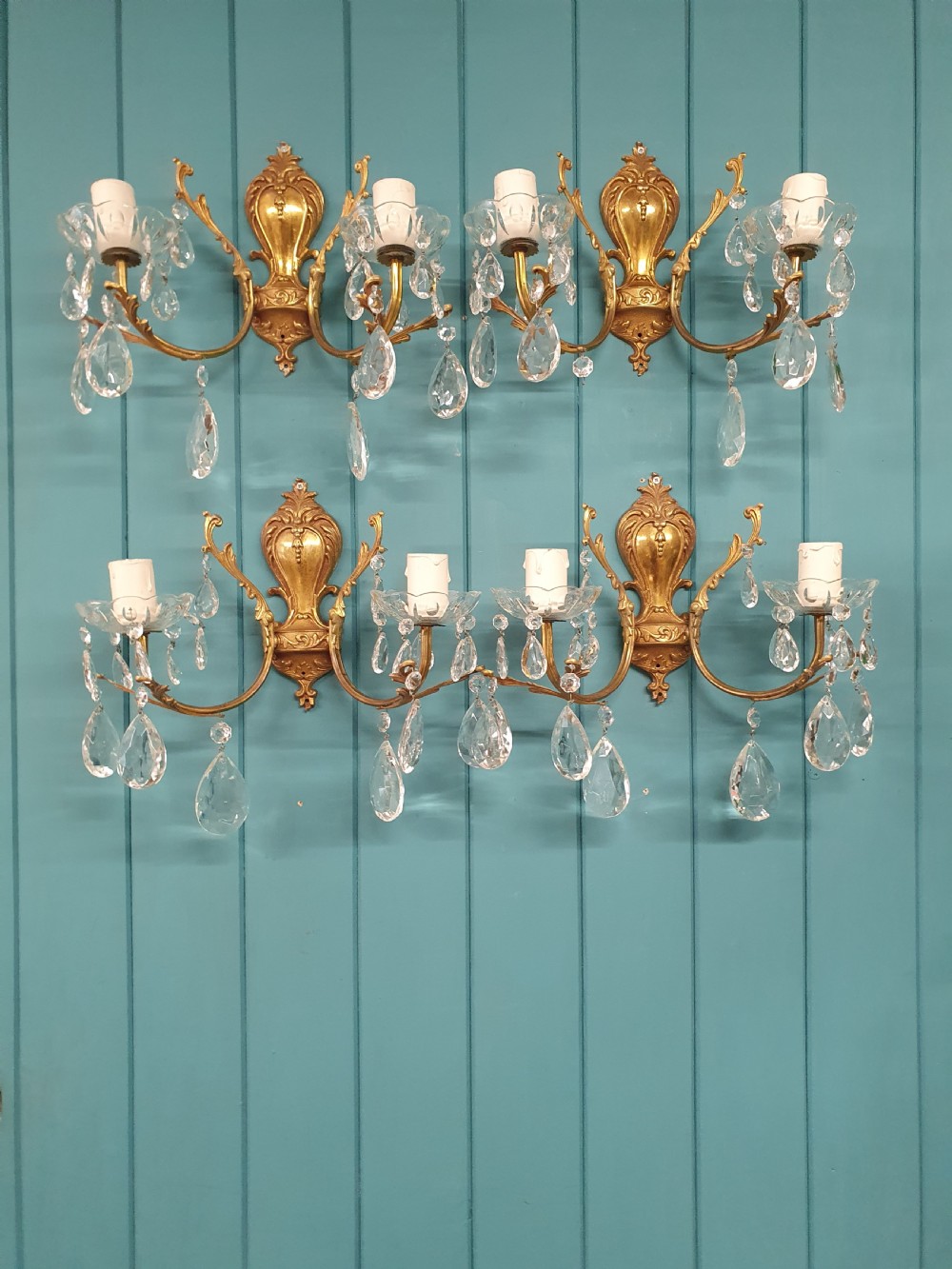 A set of four early 20th-century French Rococo revival gilt brass twin-arm wall sconces decorated with cut crystal glass droplets.
