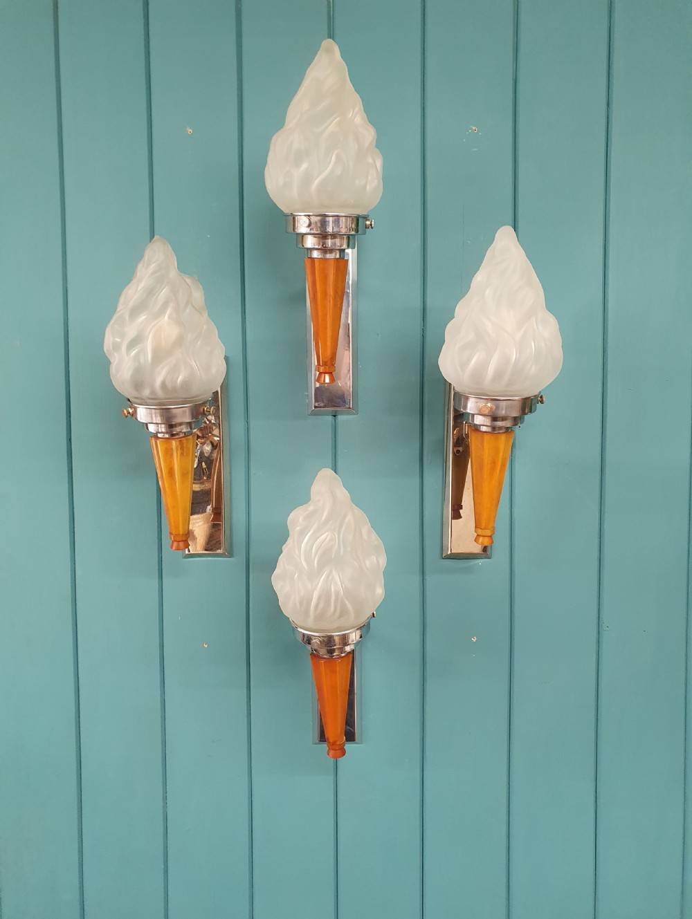 A set of four Art Deco torch-style wall lights featuring molded frosted glass flame shades set atop amber-coloured tapered stems and polished metal wall mountings.