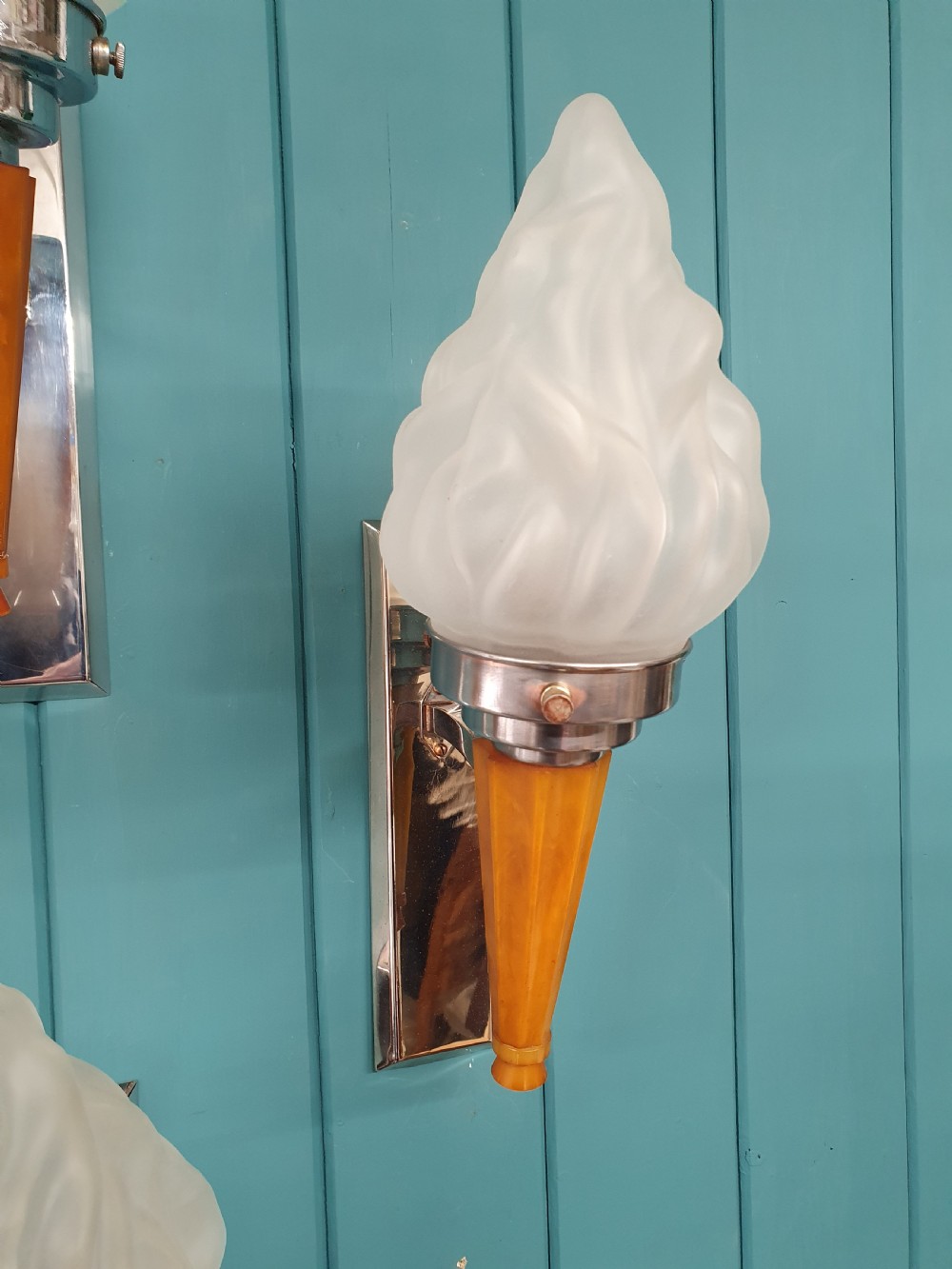 A set of four Art Deco torch-style wall lights featuring molded frosted glass flame shades set atop amber-coloured tapered stems and polished metal wall mountings. View VI