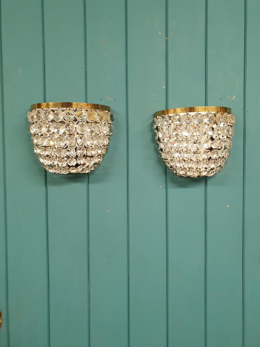 A pair of antique crystal bag wall lights featuring semi-circular pouch frames filled with faceted glass crystal beads below brass bands.