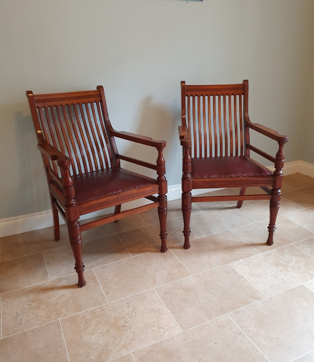 A pair of late 19th-century walnut armchairs featuring vertical slatted backrests, turned front legs, and burgundy leather seats fixed with brass studs.