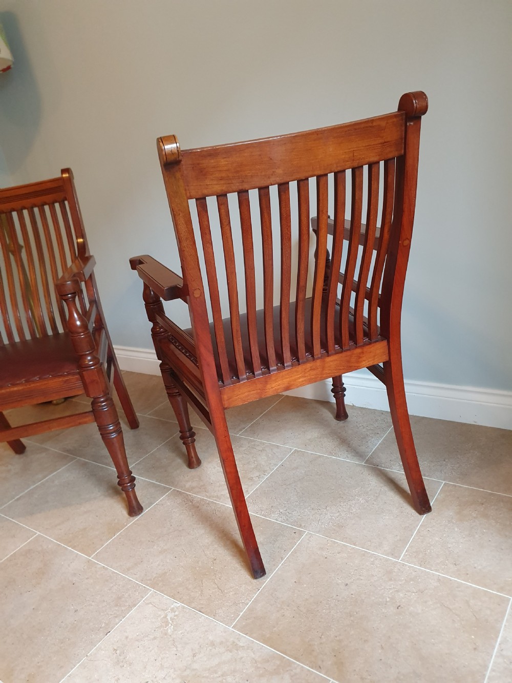 A pair of late 19th-century walnut armchairs featuring vertical slatted backrests, turned front legs, and burgundy leather seats fixed with brass studs. View II