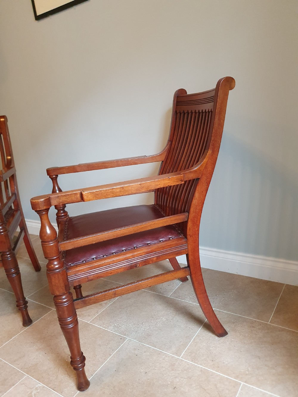 A pair of late 19th-century walnut armchairs featuring vertical slatted backrests, turned front legs, and burgundy leather seats fixed with brass studs. View III