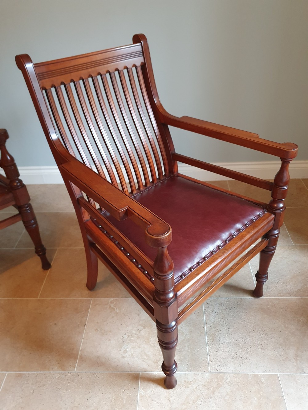 A pair of late 19th-century walnut armchairs featuring vertical slatted backrests, turned front legs, and burgundy leather seats fixed with brass studs. View IV