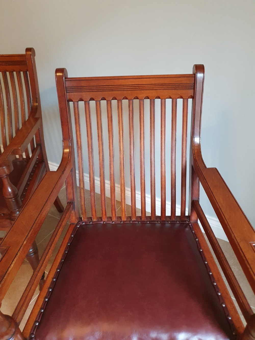 A pair of late 19th-century walnut armchairs featuring vertical slatted backrests, turned front legs, and burgundy leather seats fixed with brass studs. View V