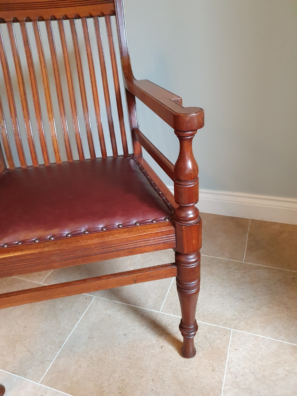A pair of late 19th-century walnut armchairs featuring vertical slatted backrests, turned front legs, and burgundy leather seats fixed with brass studs. View VI