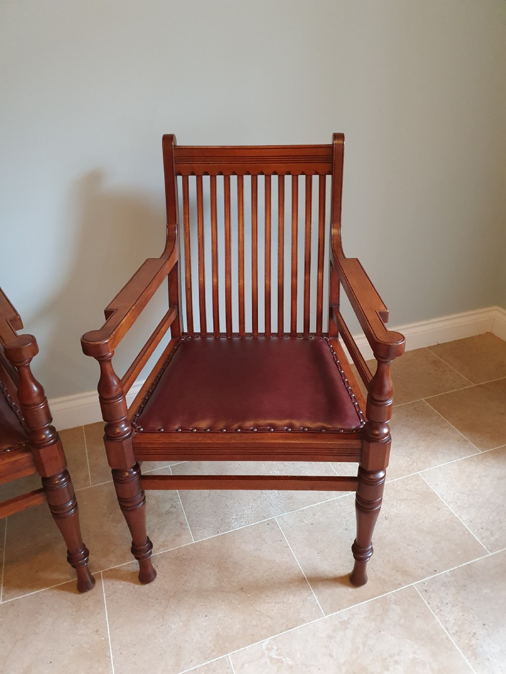A pair of late 19th-century walnut armchairs featuring vertical slatted backrests, turned front legs, and burgundy leather seats fixed with brass studs. View VII