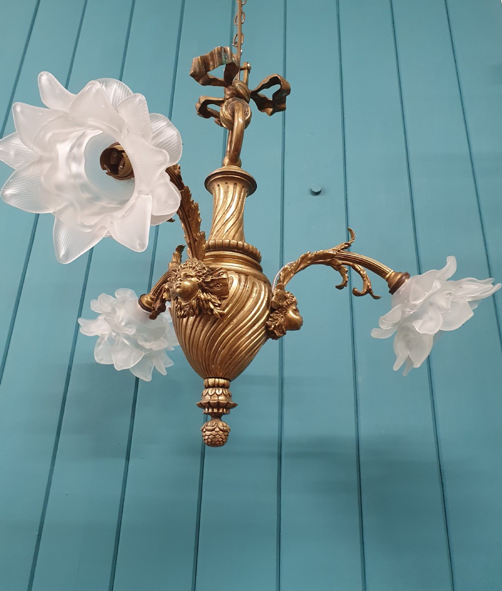A cast brass three-arm chandelier featuring cherub head reliefs on a central fluted body and floral frosted glass shades. View II
