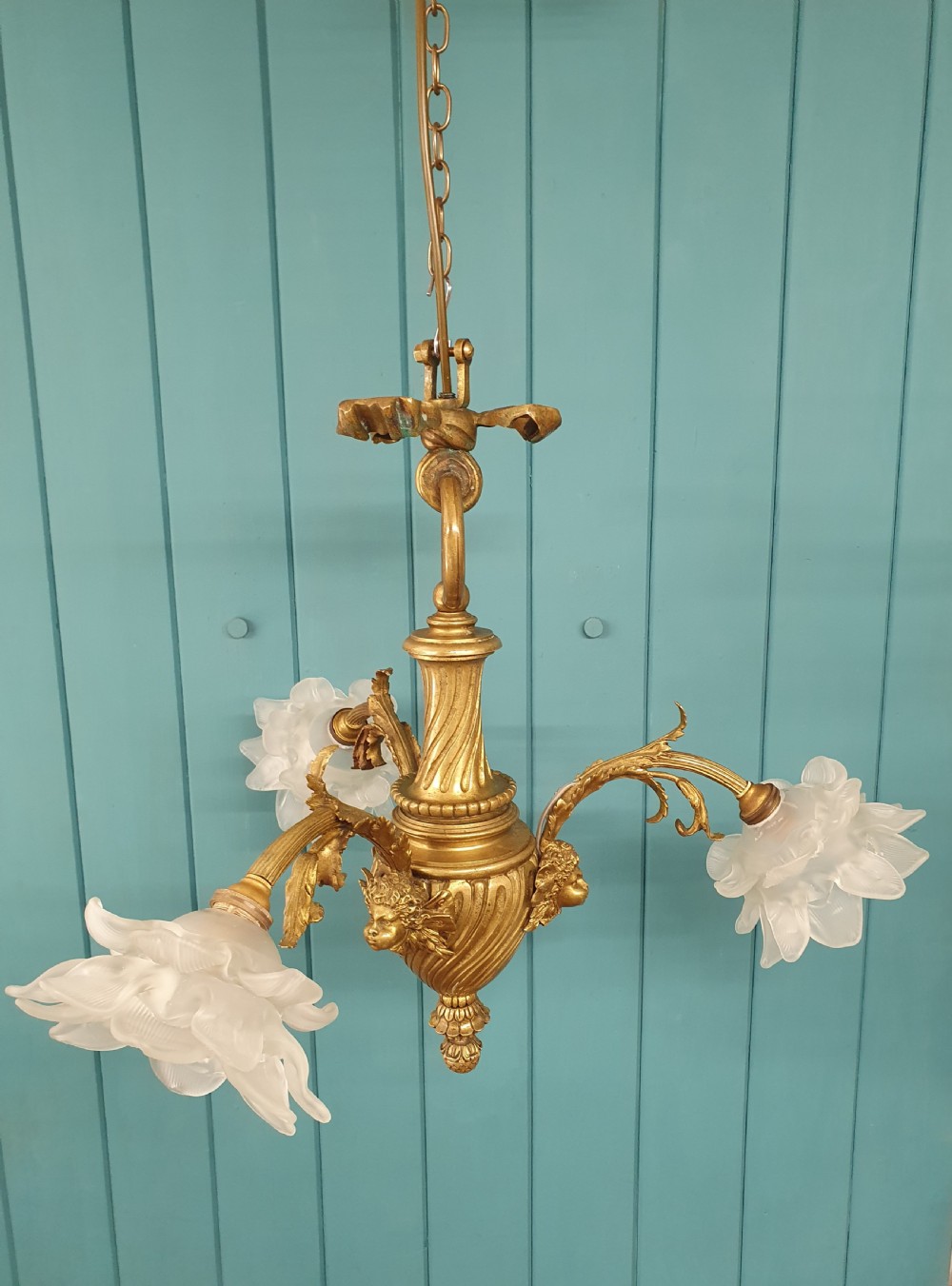 A cast brass three-arm chandelier featuring cherub head reliefs on a central fluted body and floral frosted glass shades. View III