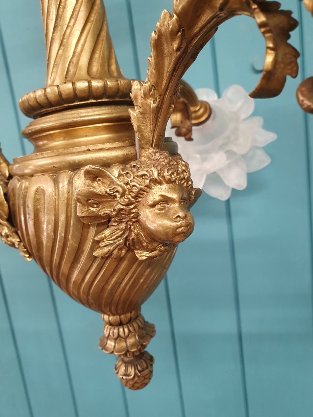 A cast brass three-arm chandelier featuring cherub head reliefs on a central fluted body and floral frosted glass shades. View IV