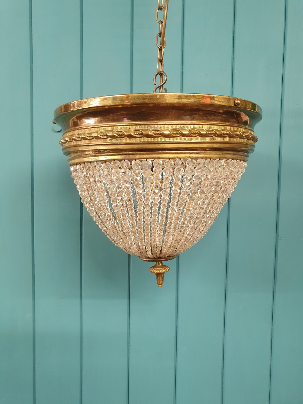 An early 20th-century ceiling light featuring a circular brass band with twisted detail above cascading strands of clear cut glass beads terminating at a brass finial.