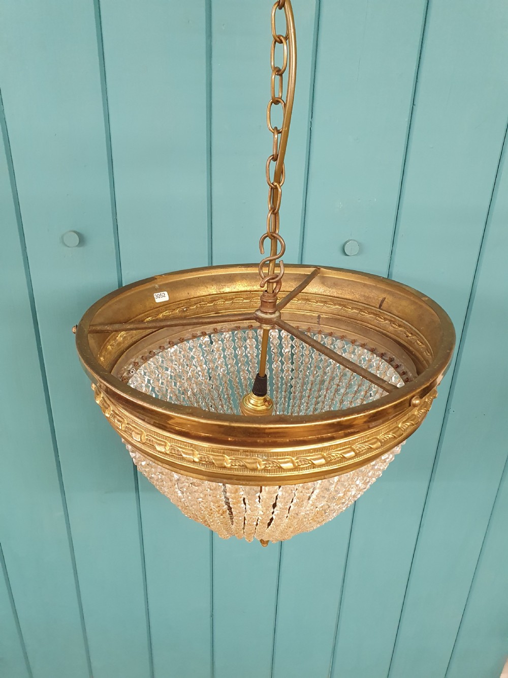 An early 20th-century ceiling light featuring a circular brass band with twisted detail above cascading strands of clear cut glass beads terminating at a brass finial. View II