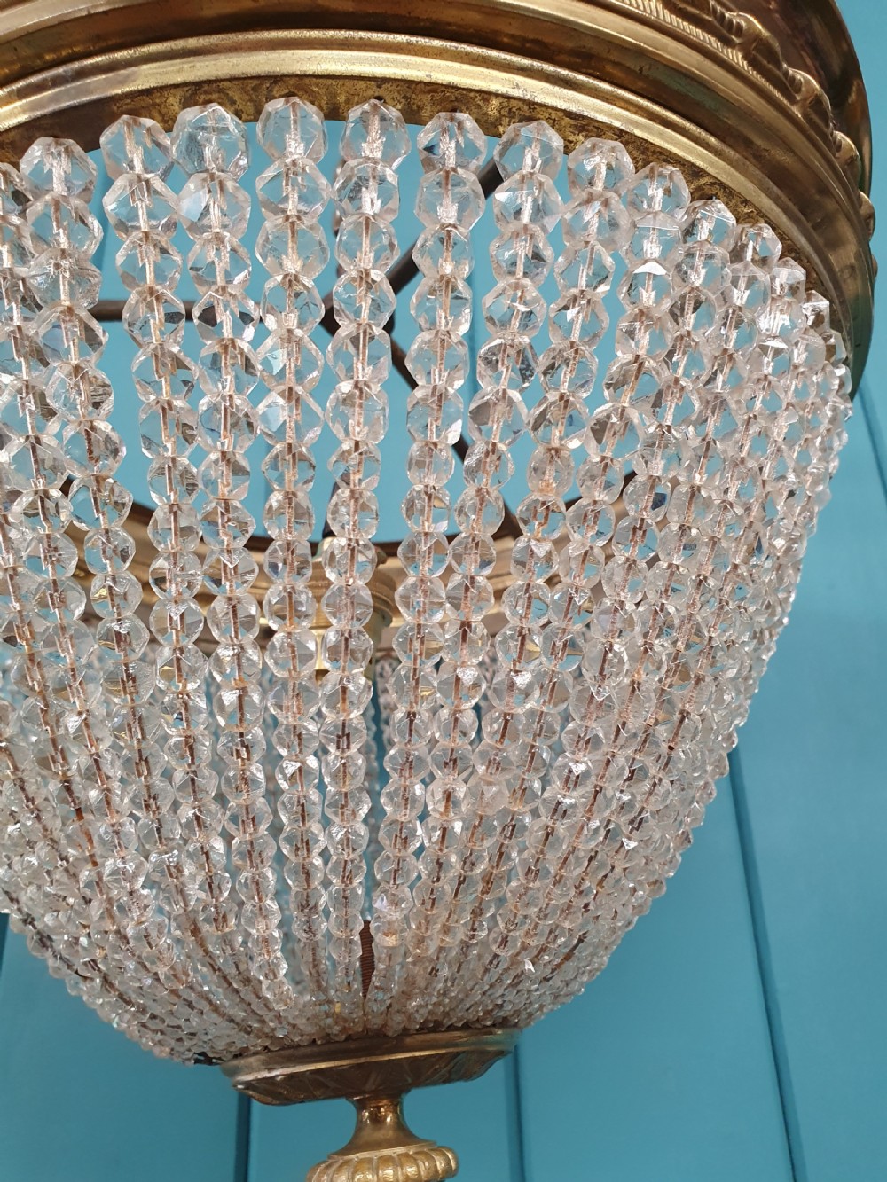 An early 20th-century ceiling light featuring a circular brass band with twisted detail above cascading strands of clear cut glass beads terminating at a brass finial. View III