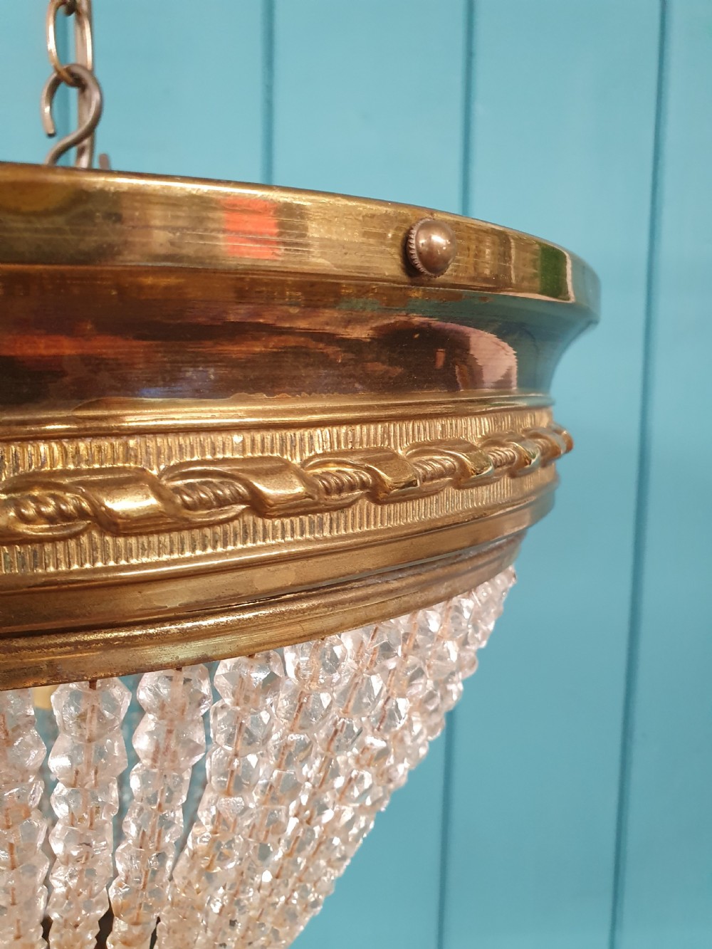 An early 20th-century ceiling light featuring a circular brass band with twisted detail above cascading strands of clear cut glass beads terminating at a brass finial. View IV