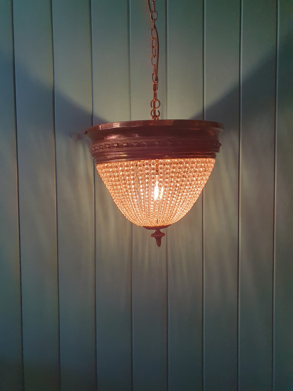 An early 20th-century ceiling light featuring a circular brass band with twisted detail above cascading strands of clear cut glass beads terminating at a brass finial. View V