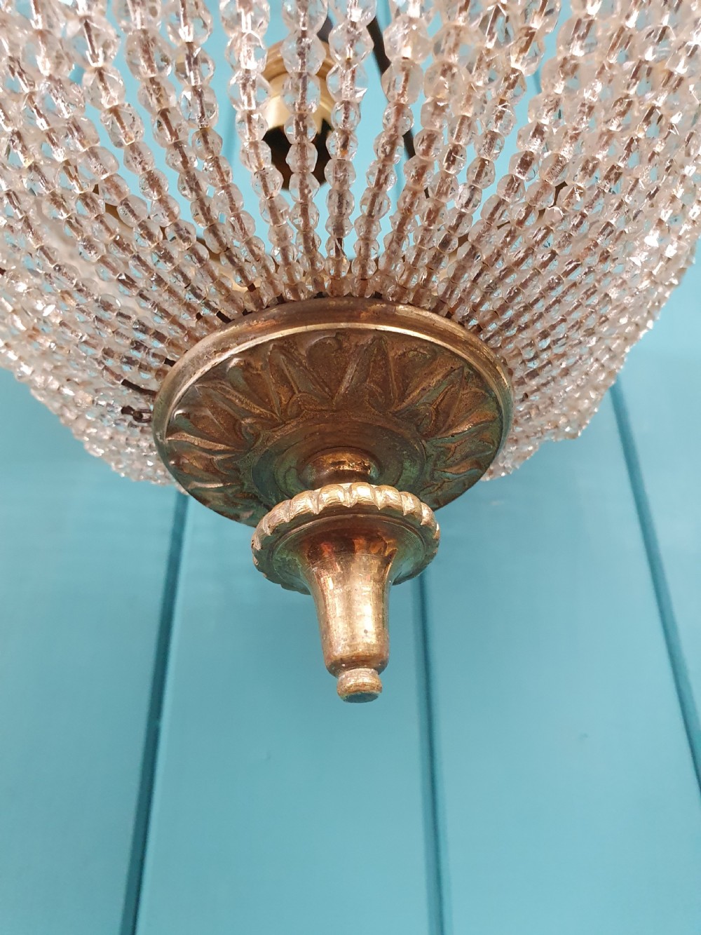 An early 20th-century ceiling light featuring a circular brass band with twisted detail above cascading strands of clear cut glass beads terminating at a brass finial. View VI